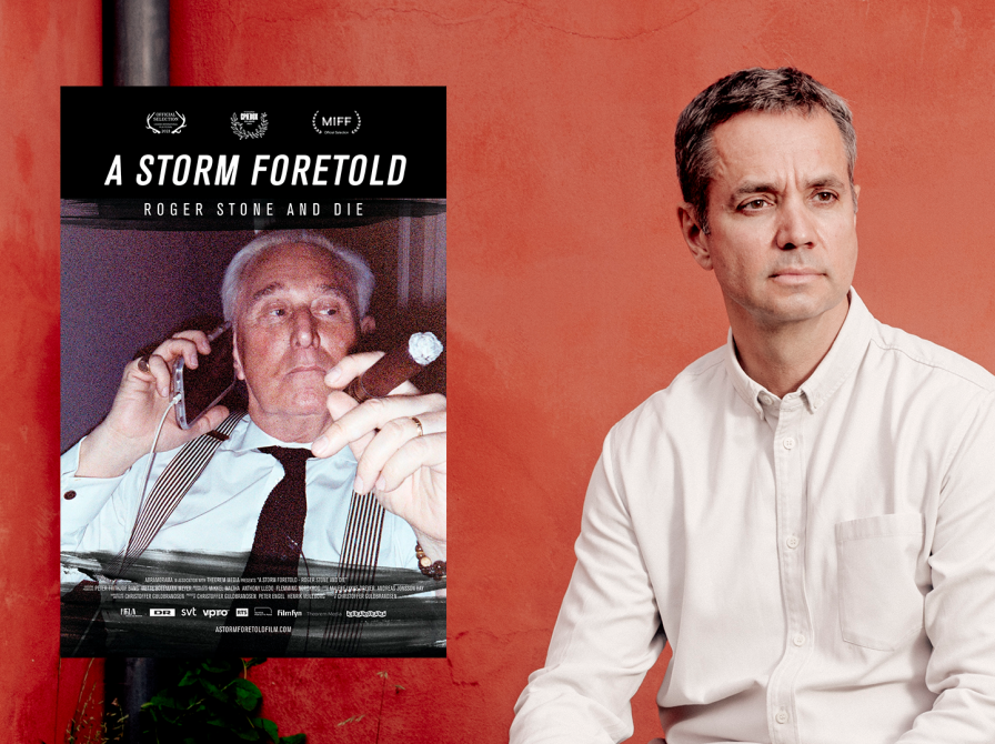 instruktør Christoffer Guldbrandsen med filmplakat for dokumentaren a storm foretold. På filmplakaten billede af Donald Trumps rådgiver Roger Stone